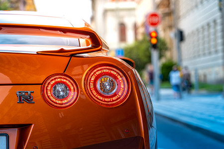 2020 年 7 月，捷克共和国布拉格 — 橙色日产天际线 GTR 的尾灯在等待绿灯的街道上