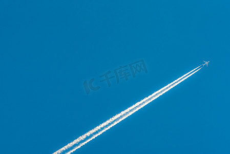 飞行痕迹摄影照片_有白色凝结轨迹的飞机。