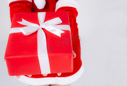 特写手女人在圣诞节拿着礼物盒，惊喜与白色背景隔离，手臂女孩在圣诞节假期或生日快乐地赠送带包装纸和白丝带的红色礼盒。