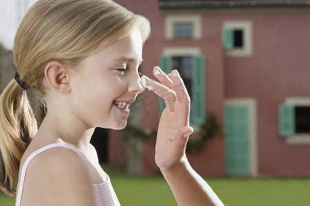 在户外给微笑的女儿鼻子涂防晒霜的手的特写侧视图