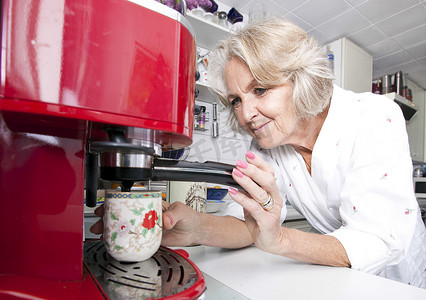 在厨房柜台用机器分发咖啡的高级女性