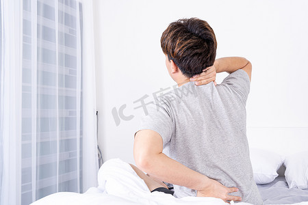 颈部疼痛摄影照片_年轻人因不舒服的床而遭受颈部和背部疼痛。