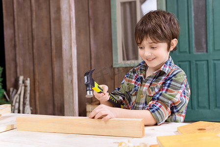 穿着格子衬衫的可爱微笑男孩在木板上钉钉子