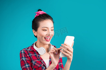 快乐的年轻亚洲女人使用智能手机站在蓝色之上。