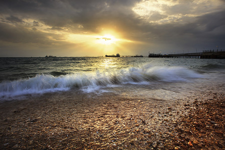 在碎石海滩上溅起海浪，映衬着夕阳西下的天空和 comme