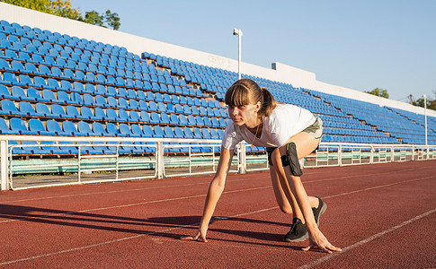 起跑摄影照片_处于起跑位置的年轻女子，准备在体育场跑道上跑步