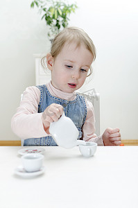 可爱的小杯子摄影照片_可爱的小女孩在家喝茶。