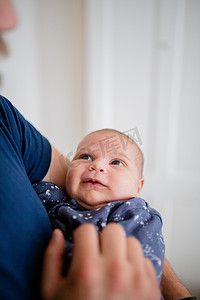 蓝色婴儿用品摄影照片_微笑的女婴在她父亲的怀里穿着蓝色连体衣