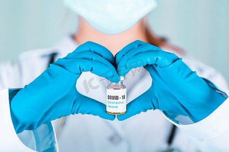 大药瓶摄影照片_身穿制服和戴面罩的女医生或护士在实验室中以一种带有 COVID-19 冠状病毒疫苗标签的心脏药瓶疫苗瓶形式进行保护