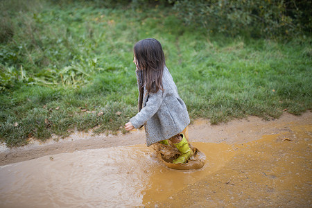 快乐的小女孩在泥泞的水坑里快乐地跳跃和飞溅