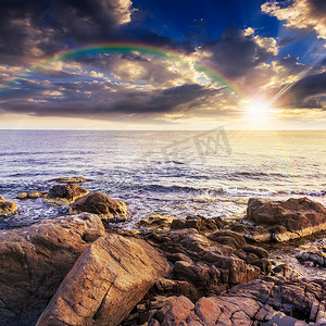 日落时海浪拍打巨石，彩虹