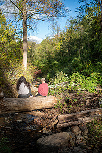 两个人在风景秀丽的森林溪流上的一根圆木上休息。