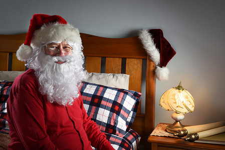 在北极，穿着红色工会套装的圣诞老人特写镜头坐在他的床边，在平安夜送完包裹后准备睡觉。