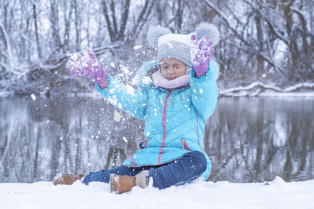 一个穿着木炭夹克的小女孩冬天在街上玩雪。孩子们在冬天在外面玩耍。