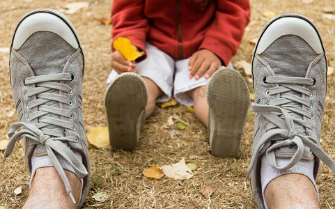 孩子坐爸爸背上摄影照片_父亲和儿子坐在田野上的运动鞋正面图