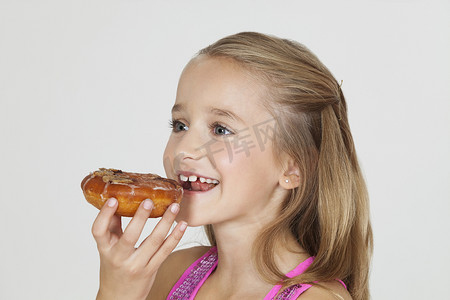 年轻女孩在灰色背景下吃甜甜圈的肖像