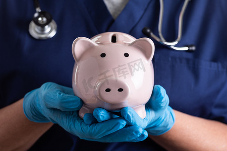 医生或护士戴着手术手套拿着存钱罐。