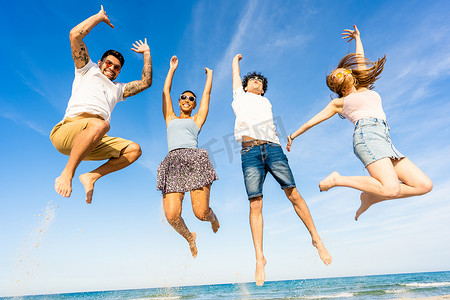 大海种族摄影照片_在热带海洋度假胜地度假时，两对快乐的多种族夫妇双臂高举天空微笑地在海水中跳跃。