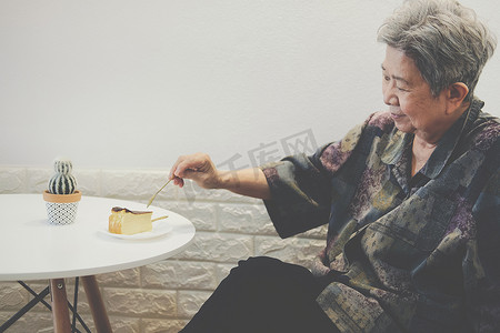 年长的亚洲老年老年妇女在餐厅吃芝士蛋糕。