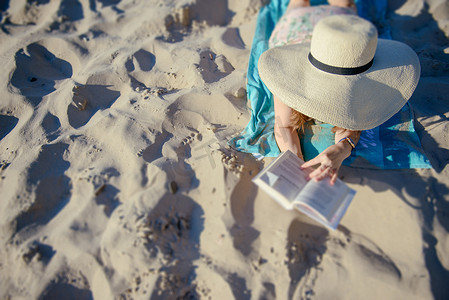 一个年轻的黑发女人在沙滩上放松的画像，正在阅读一本博