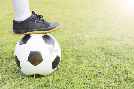 男孩脚踩在绿草地上的足球上，晚上阳光明媚。特写