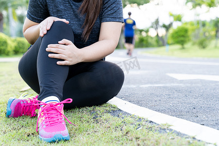 亚洲女性在公园的路上跑步时用手抓住膝盖受伤，锻炼概念造成的伤害。