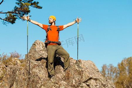 留着胡须的年轻男性正在穿越山区，旅游背包站在岩石山上，同时欣赏自然景观，在山区度过暑假