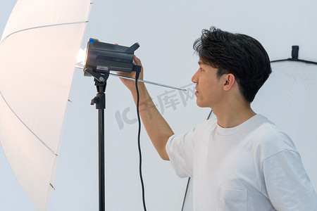亚洲摄影师正在调整摄影棚内拍摄时装模特的灯光亮度。