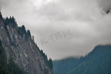 阴云密布的天空背景中，陡峭的岩石山崖被树木环绕