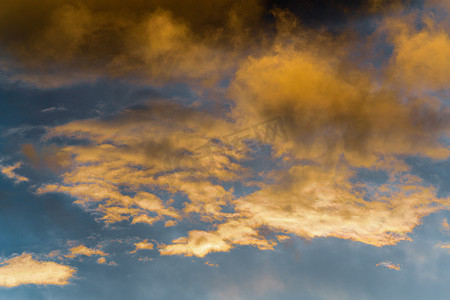 金色蓬松的云彩被日落时消失的光线照亮，而黑暗的雷云漂浮在蓝天上以改变天气。
