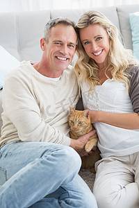 微笑的夫妇在地毯上抚摸他们的格林杰猫