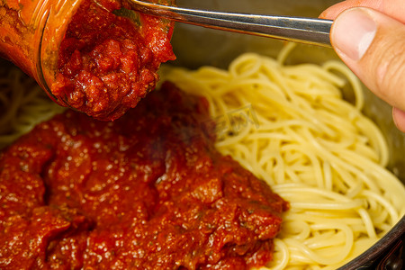 在锅里的意大利面条上加入肉酱。
