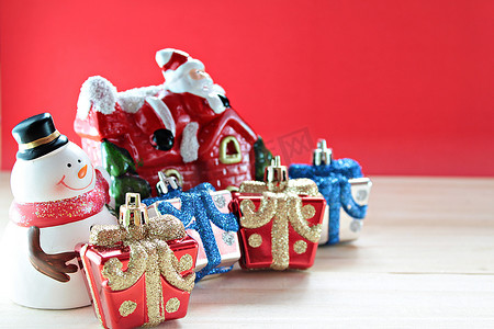 可爱的雪人、圣诞礼盒或礼物和木头上的圣诞老人屋，红色背景