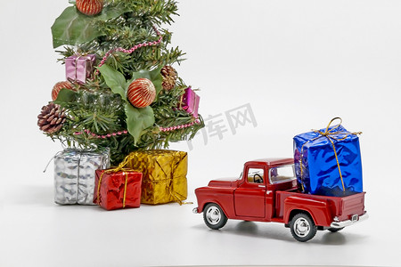 红色复古背景摄影照片_红色复古汽车玩具带着一个盒子，里面有圣诞树的礼物