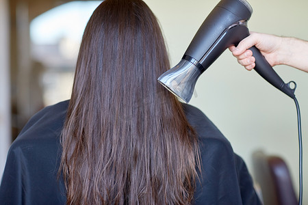 发型师吹头发摄影照片_美发师手拿扇子在沙龙吹干女人的头发