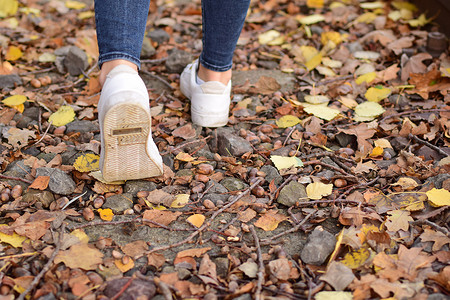 秋叶上穿蓝色牛仔裤和白鞋的步行腿