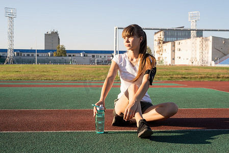 锻炼后坐在体育场喝水的年轻少女
