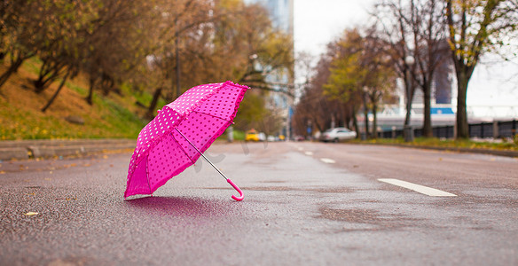 户外湿沥青上的粉红色儿童伞