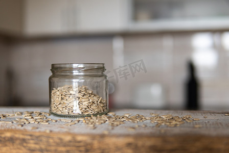 向日葵种子在一个罐子里，种子散落在白色的复古桌子上，背景是厨房。