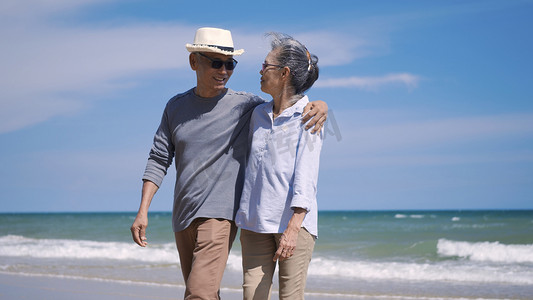 高级男女夫妇手牵着手从阳光明媚的海滩散步