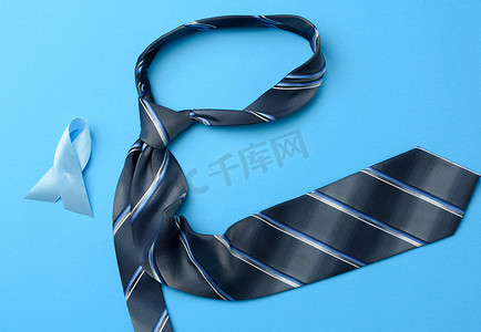 条纹丝带摄影照片_丝绸蓝色男士领带和丝带在蓝色背景上折叠成一个环