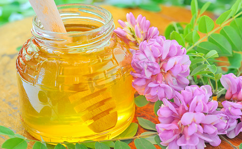 粘着摄影照片_装满蜂蜜的玻璃罐和粘着粉红色和白色相思花的蜂蜜