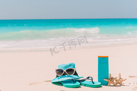 白色沙滩背景海洋上的防晒霜瓶、太阳镜、人字拖