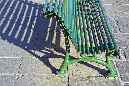 阳光照射阴影摄影照片_投下阴影的阳光照射的绿色金属长凳