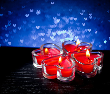 蓝色心形散景上燃烧的红色心形蜡烛
