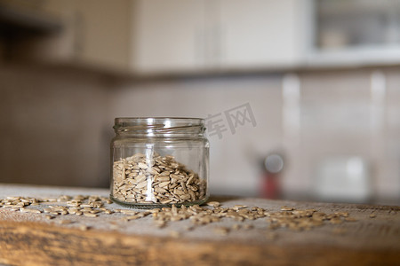 向日葵种子在一个罐子里，种子散落在白色的复古桌子上，背景是厨房。