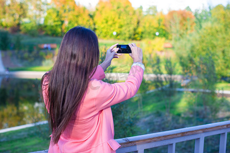 日用洗护主图摄影照片_年轻女人在秋日用手机拍照