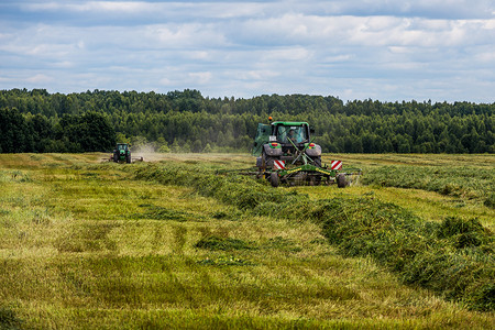 收获日摄影照片_俄罗斯图拉 — 2019 年 7 月 30 日：暴风雨前夏季田野上的绿色干草拖拉机 — 有选择聚焦的长焦镜头