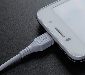 白色智能手机在黑桌上用 USB 电缆充电