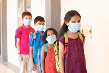 学童在课堂前排队，同时戴着医用口罩在教室外保持社交距离 — Covid-19 或学校冠状病毒安全措施的概念。